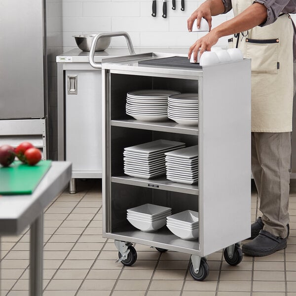 A man in an apron putting square white bowls on a Regency stainless steel utility cart.