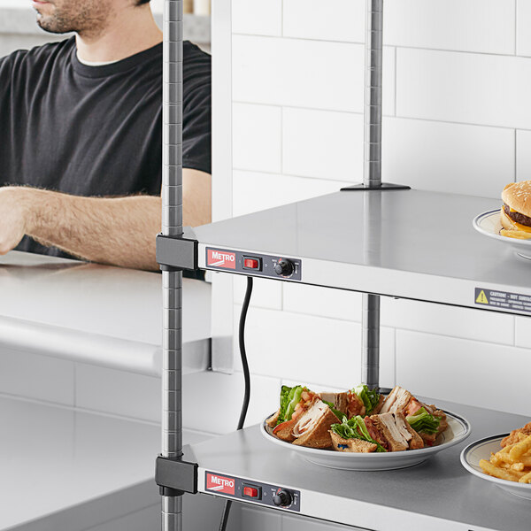 A man in a black shirt standing behind a Metro heated shelf with plates of sandwiches on it.