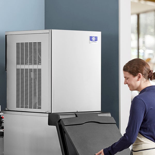 A woman standing next to a Manitowoc air cooled flake ice machine with the lid open.