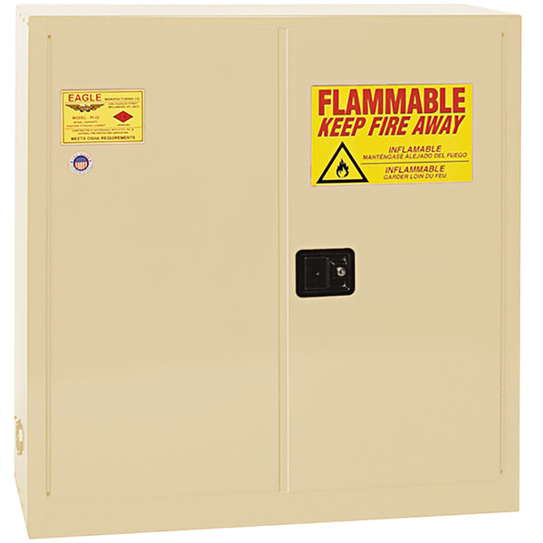 A beige Eagle safety cabinet with a yellow sign reading "Flammable - Keep Fire Away" above two black rectangular doors.