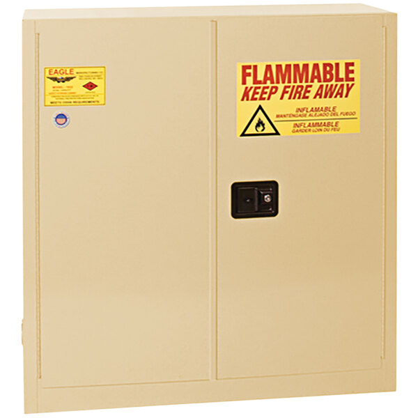 A beige Eagle Manufacturing flammable safety cabinet with a yellow and red warning sign.