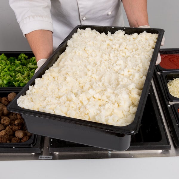 A person holding a Cambro H-Pan of mashed potatoes.