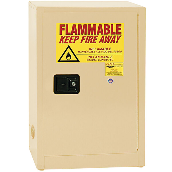 A tan metal Eagle Manufacturing safety cabinet with a yellow sign reading "Flammable Liquid" and a self-closing door.