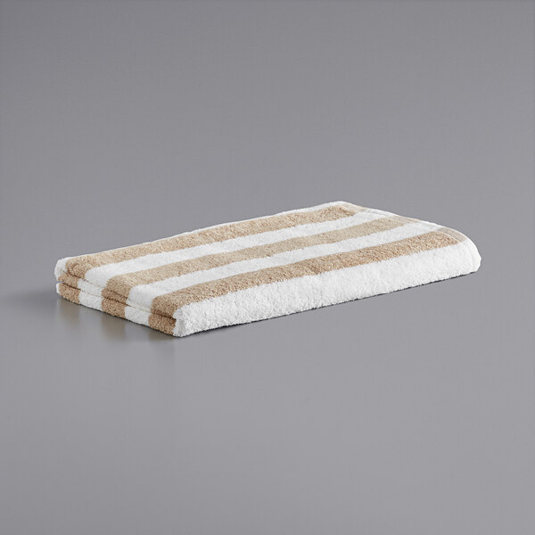 A beige striped Monarch Brands pool towel on a gray surface.