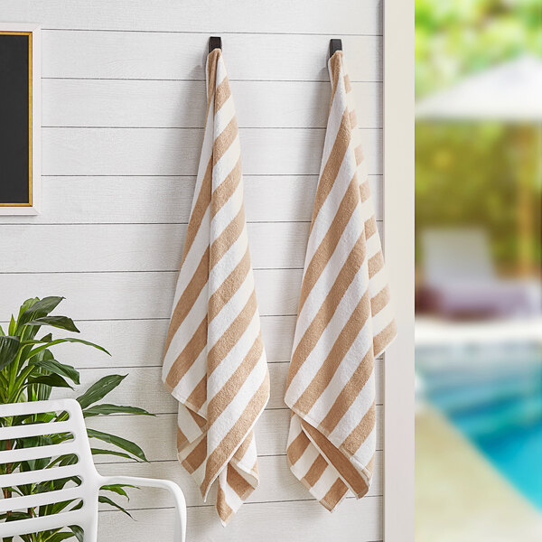 Two Monarch Brands beige striped pool towels hanging on a wall.