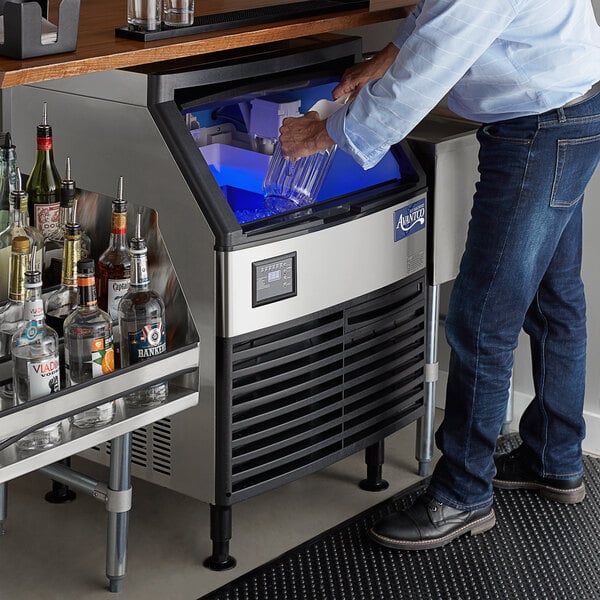 A person standing next to an Avantco undercounter ice machine.