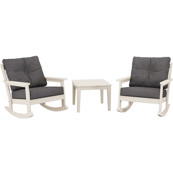 A white table with legs and two grey cushions on a table with two grey rocking chairs.