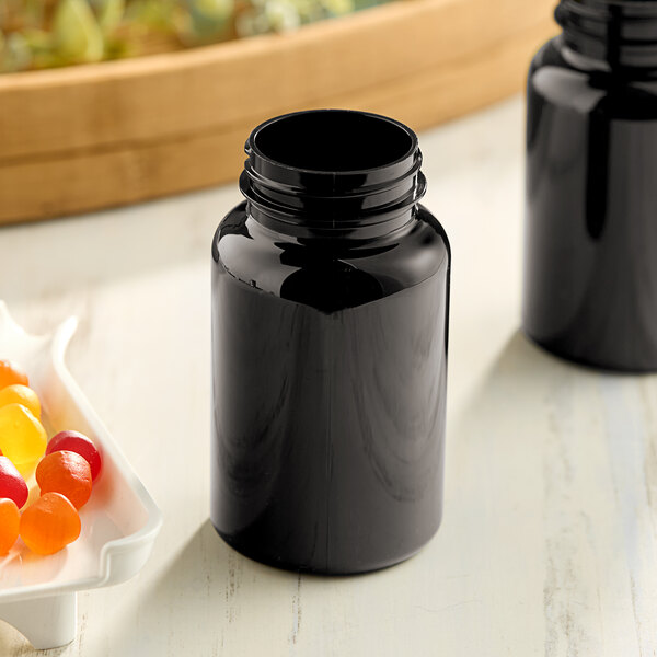 A black Dark Amber Packer Bottle with a black lid next to a bowl of jelly beans.