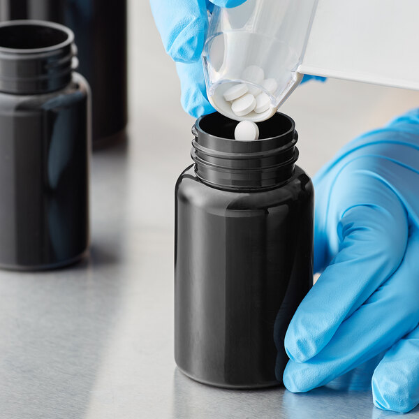 A person in blue gloves pouring liquid into a dark amber Packer bottle.