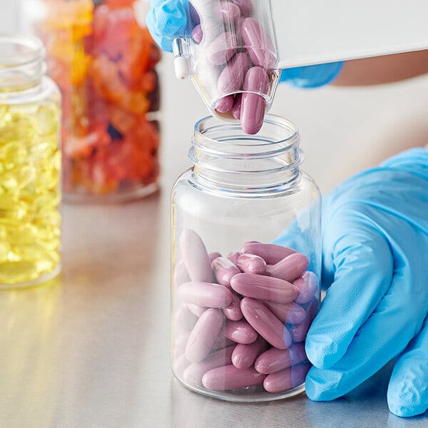 A hand in blue gloves pouring pills from a clear packer bottle.