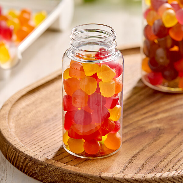A clear PET packer bottle filled with gummy candies on a wooden tray.