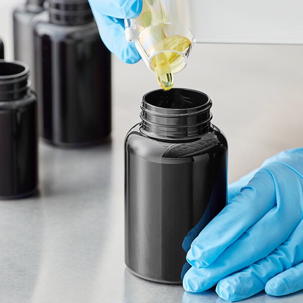A person in blue gloves pouring liquid into a dark amber 250cc packer bottle.