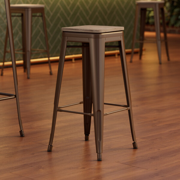 Three Lancaster Table & Seating copper barstools with gray wood seats on a wood floor.