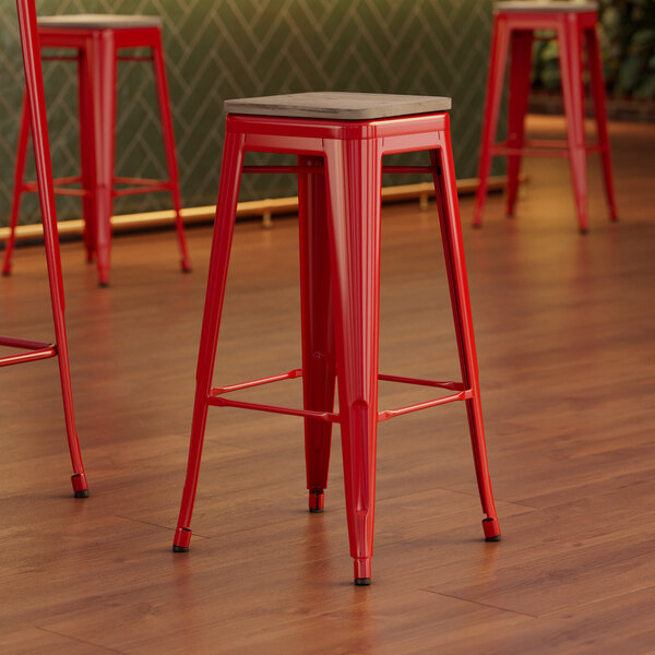 A close-up of a red Lancaster Table & Seating backless barstool with a gray wood seat.