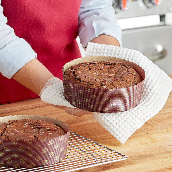 A woman holding a brown Novacart paper baking mold with a brown cake inside.