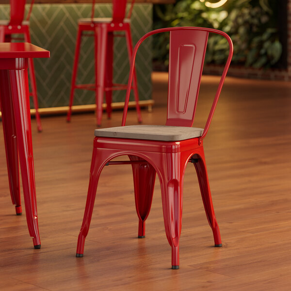 A Lancaster Table & Seating red metal chair with a gray wood seat in a restaurant dining area.