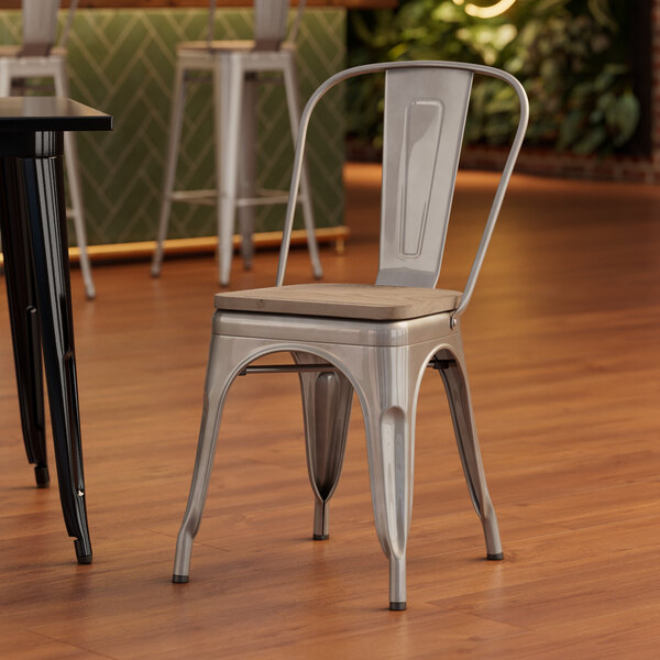 A Lancaster Table & Seating silver metal cafe chair with a gray wood seat sits at a table.