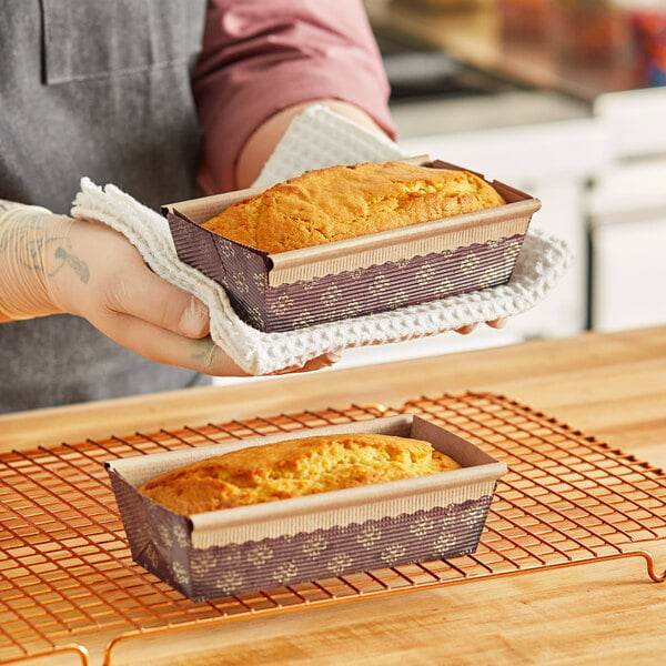 A woman holding two Novacart bread loaves in paper pans.