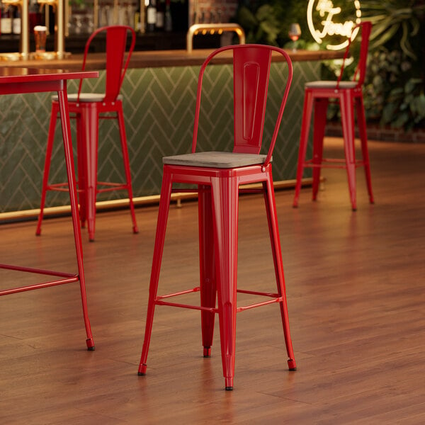 A Lancaster Table & Seating Ruby Red Cafe Barstool with Gray Wood Seat at a table in a bar.