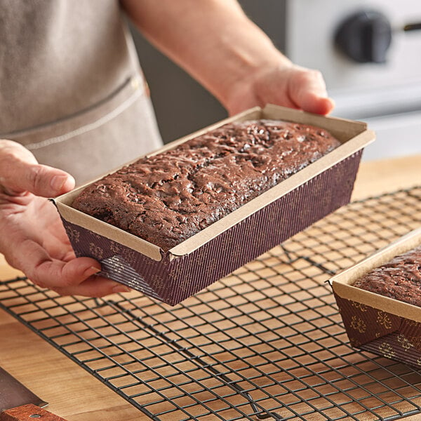 A hand holding a loaf of chocolate cake in a Novacart corrugated kraft paper bread loaf pan.