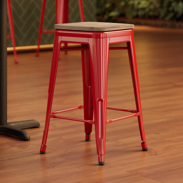 A Lancaster Table & Seating red metal backless counter height stool with a gray wood seat.