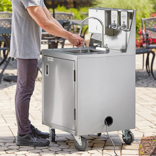 A person washing their hands in a stainless steel sink on a Regency portable sink cart.