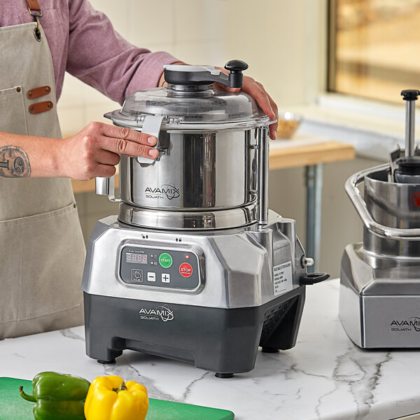 A person using an AvaMix stainless steel bowl and food processor on a counter in a professional kitchen.