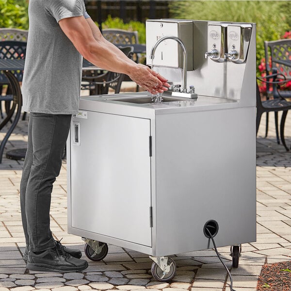 A man washing his hands in a stainless steel portable sink.