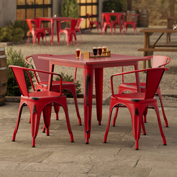 A Lancaster Table & Seating distressed ruby red table with 4 chairs outside on a patio.