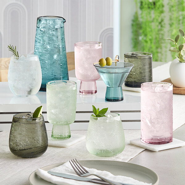 A table with different colored glasses and utensils including Acopa Mauve Beverage Glasses.