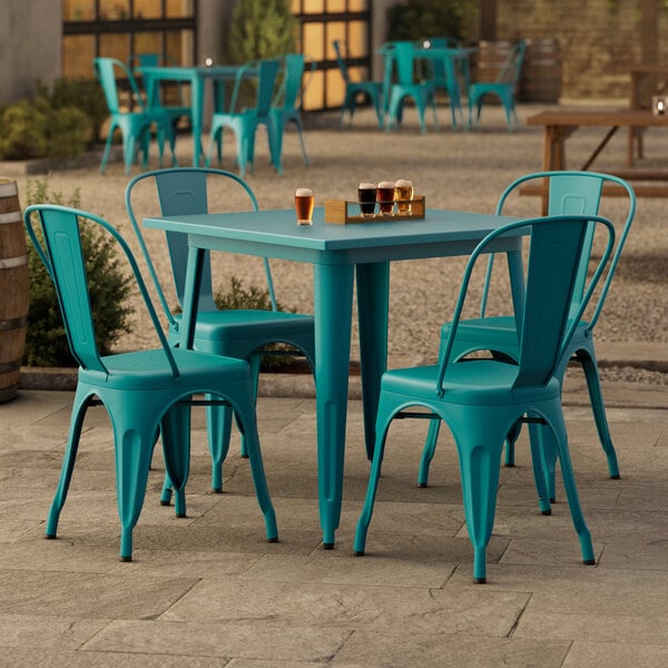 A Lancaster Table & Seating teal table with four chairs on an outdoor patio.