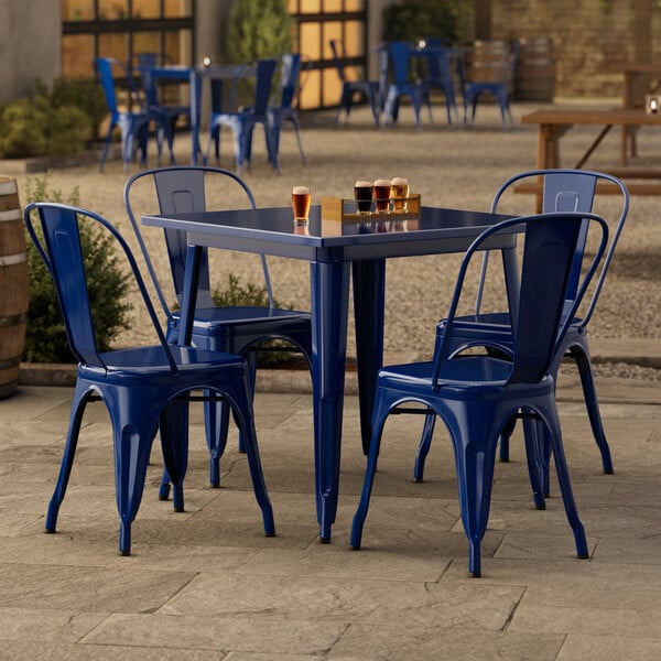 A blue metal Lancaster Table & Seating outdoor table with four chairs on a patio.