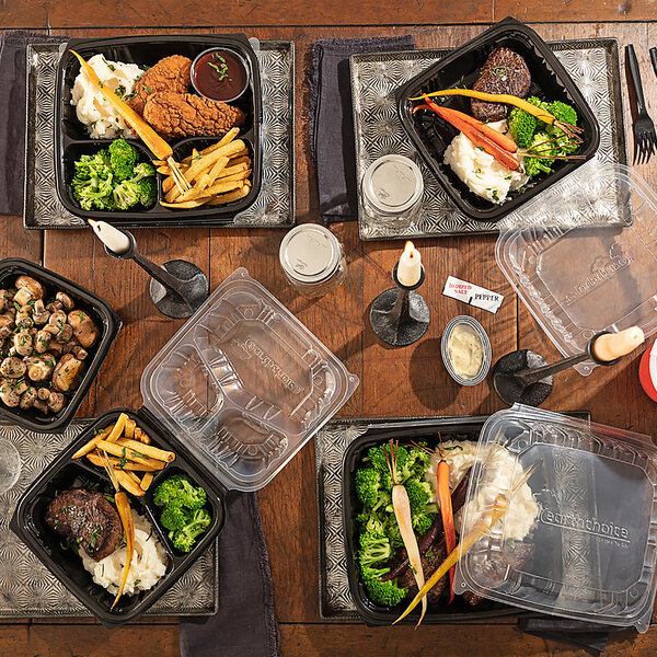 A table with black Pactiv Earthchoice plastic containers of food on it.