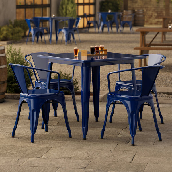 A blue metal Lancaster Table & Seating outdoor table with four blue chairs on a stone patio.
