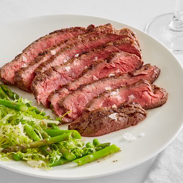 A plate with Warrington Farm Meats flank steak and vegetables on a white table.