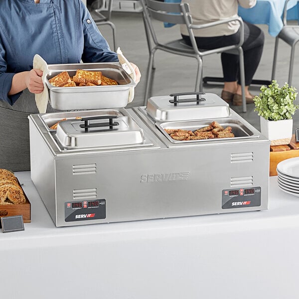 A woman using a ServIt countertop food warmer to serve food at an outdoor buffet.