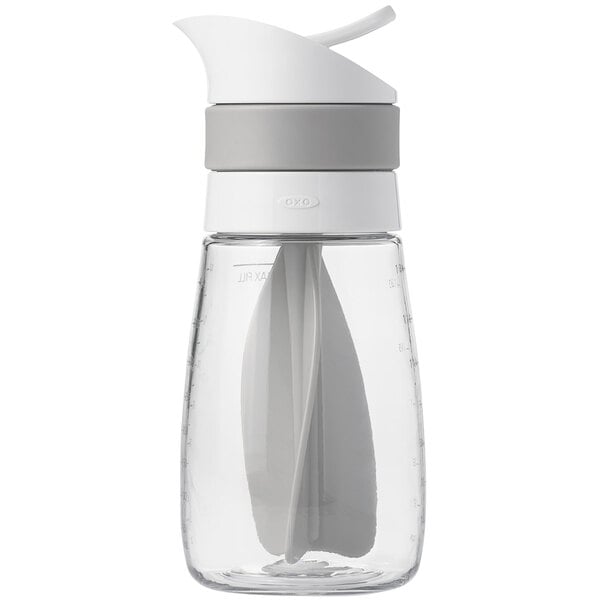 An OXO white and gray salad dressing mixer with a spoon in it.