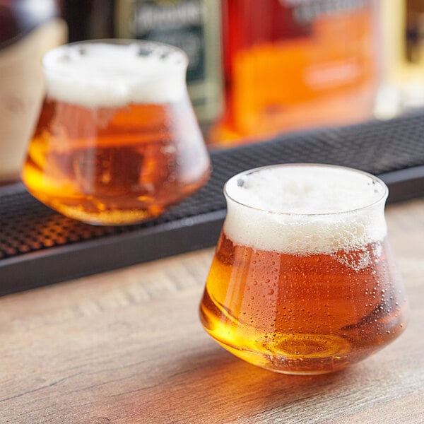 Two Rastal Teku beer glasses on a table with beer and foam.