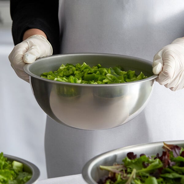 A person in gloves holding a close-up of a stainless steel mixing bowl filled with salad.