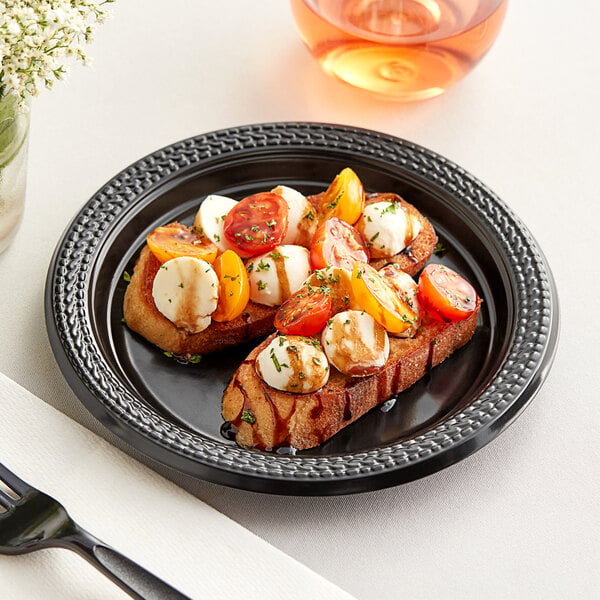 A Fineline black polypropylene plate with food on it on a table.