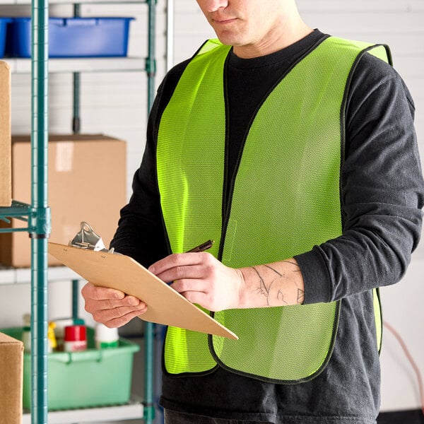 A lime high visibility mesh safety vest being worn by a person in a warehouse setting.