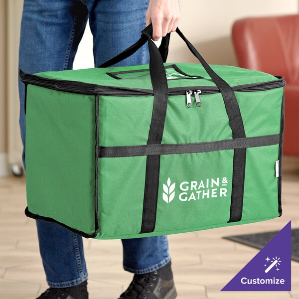 A person is holding a large green insulated bag with black handles and a zipper, featuring the text 'GRAIN & GATHER' and a leaf logo on the side.