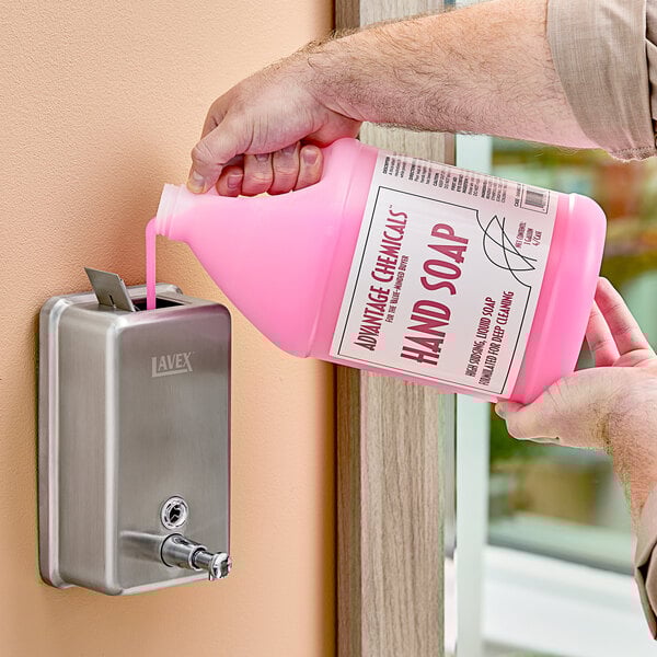 A person pouring pink liquid from a bottle into a soap dispenser.
