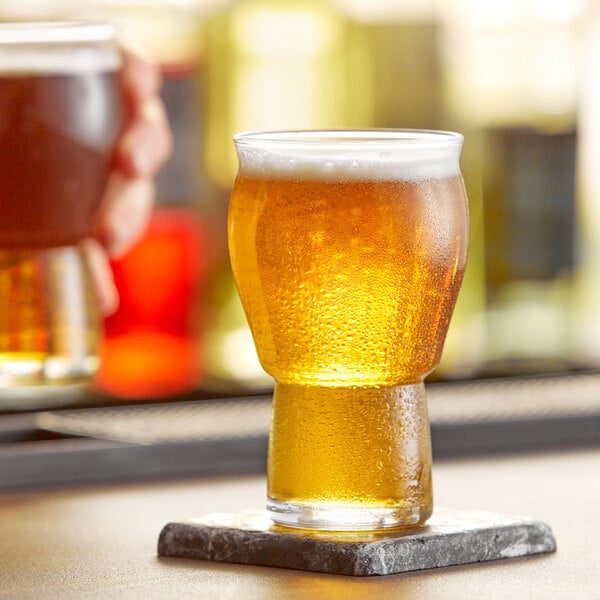 A Rastal Craft Master Grand beer glass of beer on a coaster on a table in a bar.