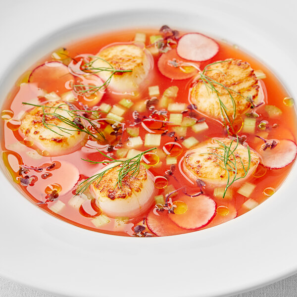 A bowl of soup with scallops and vegetables made with Les Vergers Boiron Sicilian Blood Orange fruit puree.