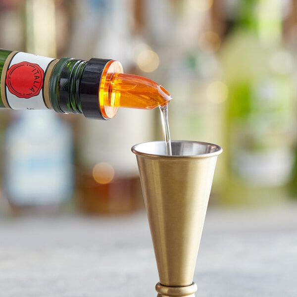 A person using a Choice Short Free Flow Amber Liquor Pourer to pour liquid into a gold cup.