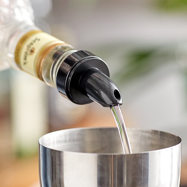 A person using a Choice Short Free Flow black liquor pourer to pour liquid into a metal cup on a counter.