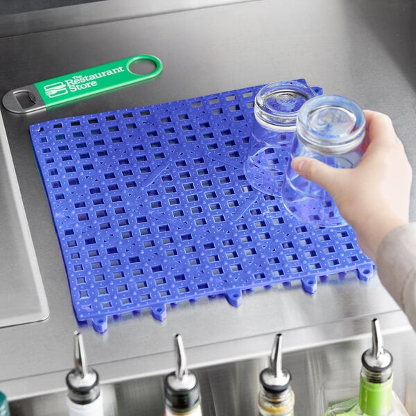 A person pouring a liquid into a blue Choice interlocking bar mat on a counter.