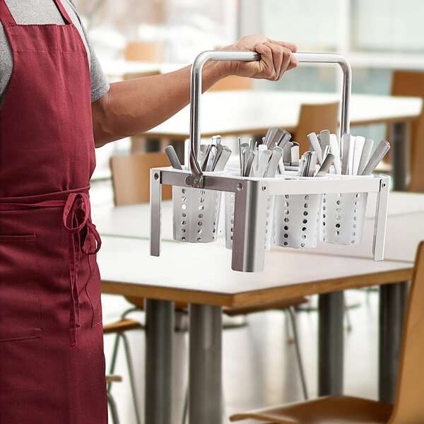 A man holding a Choice metal basket with white plastic cylinders filled with utensils.