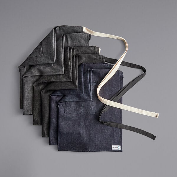 Acopa Kennett grey and black denim aprons stacked on a table.